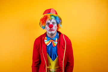 A pensive, sad adult clown on a vibrant yellow background.