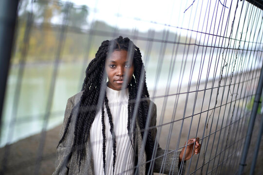 Woman with braided hair standing behind a wire fence, looking pensively at the camera, Brandenburg, Germany