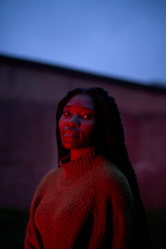 Woman in a knitted sweater looking up illuminated by a soft red light against a twilight sky, Brandenburg, Germany