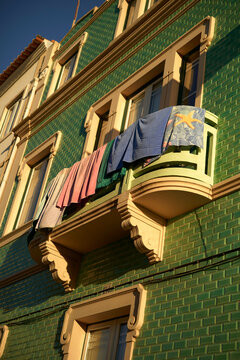 Colorful laundry hangs to dry on the balcony of a green tiled building under a clear sky, Portugal