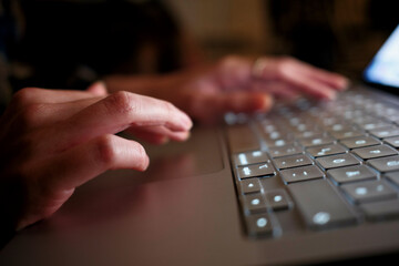 Close-up of hands typing on a laptop keyboard with a blurred background.
