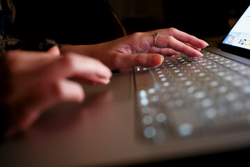 Close-up of hands typing on a laptop keyboard in a dimly lit environment.