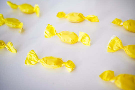 Candy wrapped in yellow paper arranged ona white surface