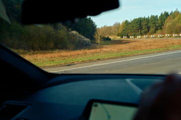 View from a car's interior overlooking a highway with a line of trucks in the distance and surrounding greenery, Highlands, Scotland