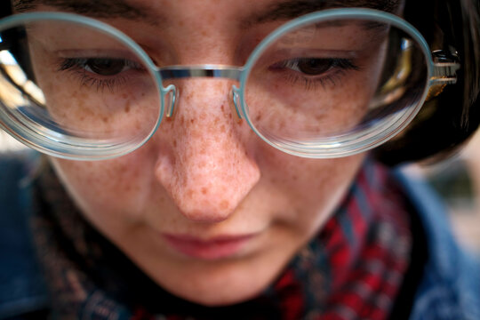 Close-up of a young woman with freckles wearing round glasses looking downwards.