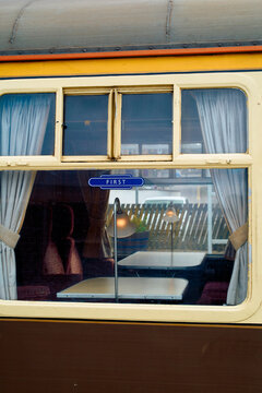 Vintage train carriage window with a First'class sign, showing plush seating and curtains inside, Scotland