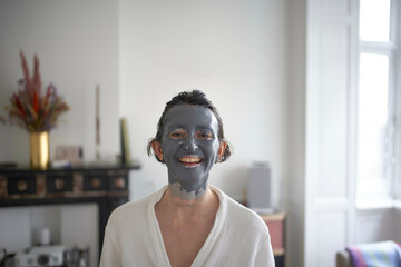 Smiling young woman with a facial mask sitting indoors.