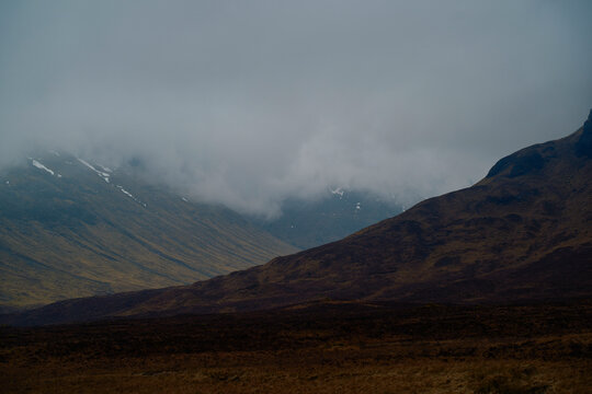 A misty mountain peak with its summit shrouded by low-hanging clouds, set against a somber sky, Scotland