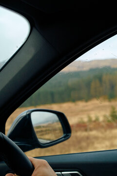 View from inside a car showing a side mirror and a window with raindrops, overlooking a blurred landscape, Scotland