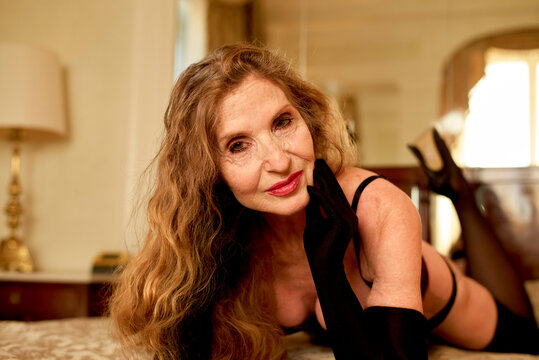 An elegant woman in a black dress and gloves poses on a couch with a warm smile and confident demeanor, Rome, Italy