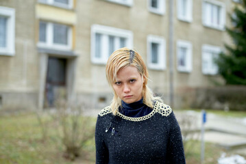 Young blond woman with a perturbed expression standing in front of a residential building, East Germany