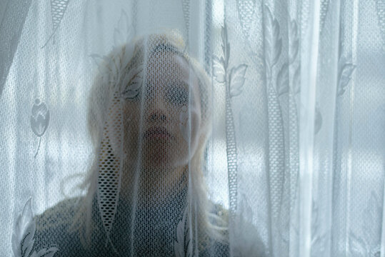 Woman with blonde hair seen through a sheer patterned curtain, East Germany