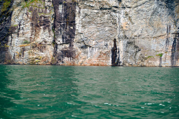 Green ocean water at the base of a towering cliff with rugged textures, Geirangerfjord, Norway
