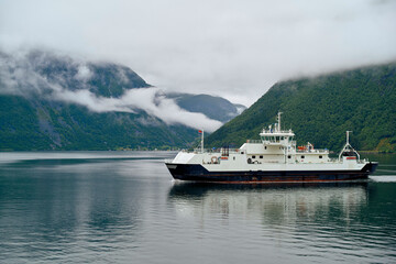 A ferry boat on a calm fjord with low-hanging clouds over the surrounding mountains, Norway