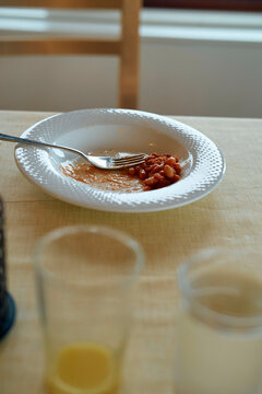 Half-eaten meal of beans on a white plate with a fork and two empty glasses on a wooden dining table, Norway