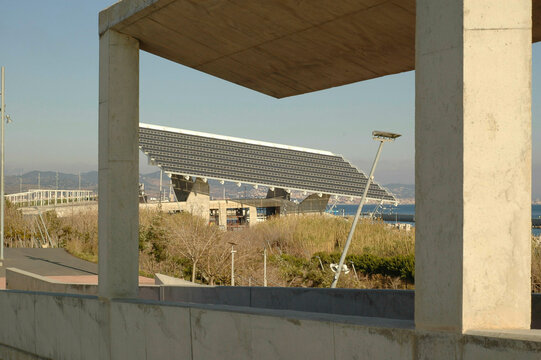 Concrete architectural structure framing a view of a solar panel array with clear skies and sea in the background, Barcelona, Spain