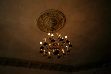 Anti0ue chandelier with candles lit against a ceiling with intricate mouldings in a dimly lit room, Poznan, Poland
