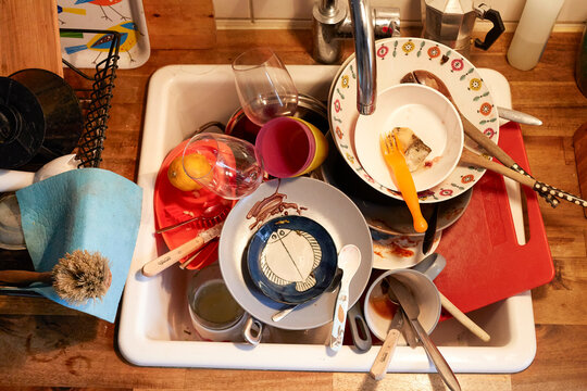 A sink full of dirty dishes, including cups, plates, and utensils with food residue, Germany