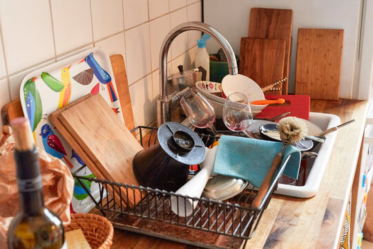 A full kitchen sink dish rack with various dishes, glasses, utensils, and cutting boards, Germany