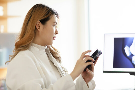 Professional woman examines a camera in a brightly lit office with a computer screen in the background.