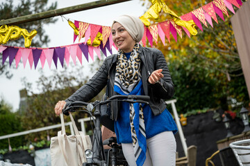 Smiling woman in a hijab riding a bicycle past colorful banners at a garden party.
