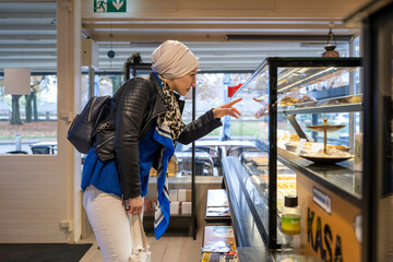 Woman in a headscarf pointing at pastries in a bakery display case, Netherlands