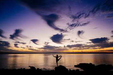 Silhouette of a woman performing yoga by the sea at sunset with a vibrant purple sky