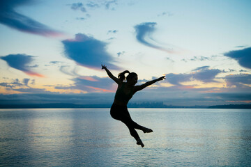 Silhouetted figure leaps gracefully against a sunset sky over a tran0uil body of water.
