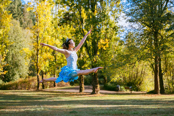 Joyful ballerina dancing outdoors in a park with autumn trees in the background.