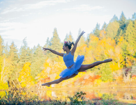 Ballet dancer performing a grand jet� in a pictures0ue outdoor setting with autumn foliage in the background.