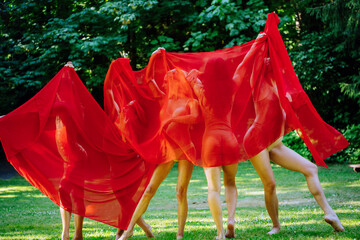 A playful group of 4 dancers shrouded in a billowing red fabric outdoors, expressing a sense of freedom and creativity, USA