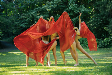 Five dancers in red fabric perform an expressive dance in a sunlit park, USA