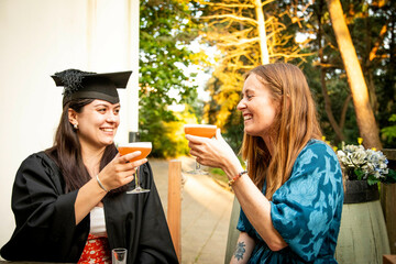 Graduation celebration outdoors with two women toasting with drinks at golden hour, Bournemouth, Dorset UK