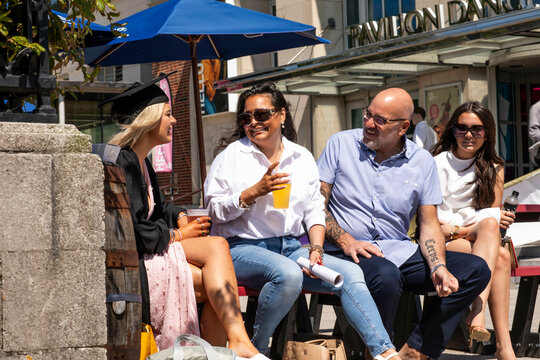 Family enjoying a sunny day outside a cafe with drinks and engaging in a lively conversation over graduate day and the daughter's diploma, Bournemouth, Dorset UK 