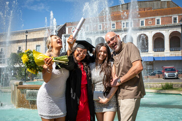 Graduation celebration with four joyous people in front of a fountain, one in a cap and gown holding a diploma and flowers, Bournemouth, Dorset UK