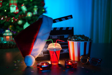 Merry Christmas and New Year Holidays Scene. Santa Claus Hat, Movie Clapperboard, Christmas Tree, Garland, Neon Lights, Cinema Popcorn, and 3D Glasses. Perfect Setting for Holiday Movie Nights at Home