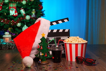 Merry Christmas and New Year Holidays Scene. Santa Claus Hat, Movie Clapperboard, Christmas Tree, Garland, Neon Lights, Cinema Popcorn, and 3D Glasses. Perfect Setting for Holiday Movie Nights at Home