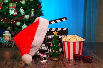 Merry Christmas and New Year Holidays Scene. Santa Claus Hat, Movie Clapperboard, Christmas Tree, Garland, Neon Lights, Cinema Popcorn, and 3D Glasses. Perfect Setting for Holiday Movie Nights at Home