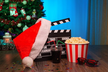Merry Christmas and New Year Holidays Scene. Santa Claus Hat, Movie Clapperboard, Christmas Tree, Garland, Neon Lights, Cinema Popcorn, and 3D Glasses. Perfect Setting for Holiday Movie Nights at Home
