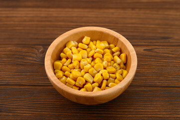 Golden corn kernels in a rustic wooden bowl on a dark wooden table, creating a warm and natural presentation of this wholesome vegetable.
