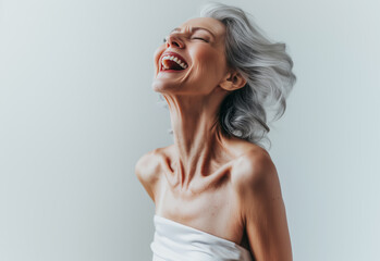 Fototapeta premium Joyful portrait of an elderly Caucasian woman with silver hair, laughing freely and exuding confidence, set against a minimalist white background