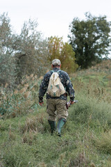 Mature hunter man holding a shotgun and walking through a field