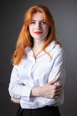 Portrait of a red-haired girl in a white shirt. Woman smiling in studio against gray background.