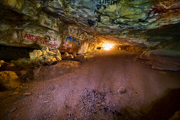 Graffiti Adorned Cave Interior with Natural Light Exit View