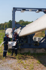 Engineers in safety gear conduct a detailed inspection of wind turbine blades at a construction site. Large blades are placed on the ground, highlighting the renewable energy technology.