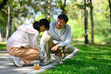 Caring young adult daughter tying her father shoelaces during their walk in the park