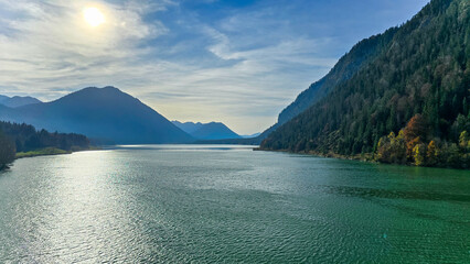 Beautiful view of Sylvensteinsee and Alpine foothills in autumn evening. Green water and yellow-red trees.