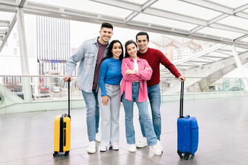 A happy couple stands with two friends in an airport terminal, ready for their weekend getaway....