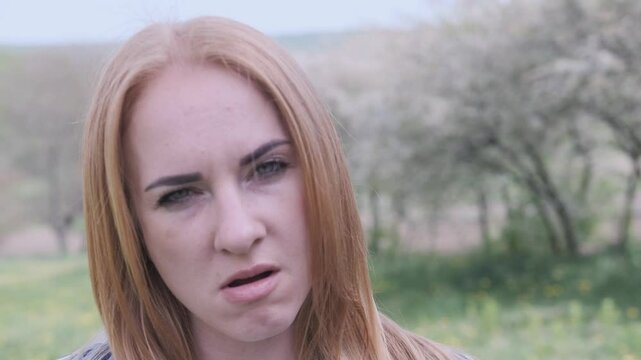 Red haired woman making various irritability faces in slow motion against a picturesque rural backdrop during springtime