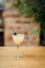 A classic gin-based cocktail with Chartreuse liqueur, Maraschino liqueur, and fresh lime juice, garnished with a cherry on top on a wooden bar counter against brick wall vertical image